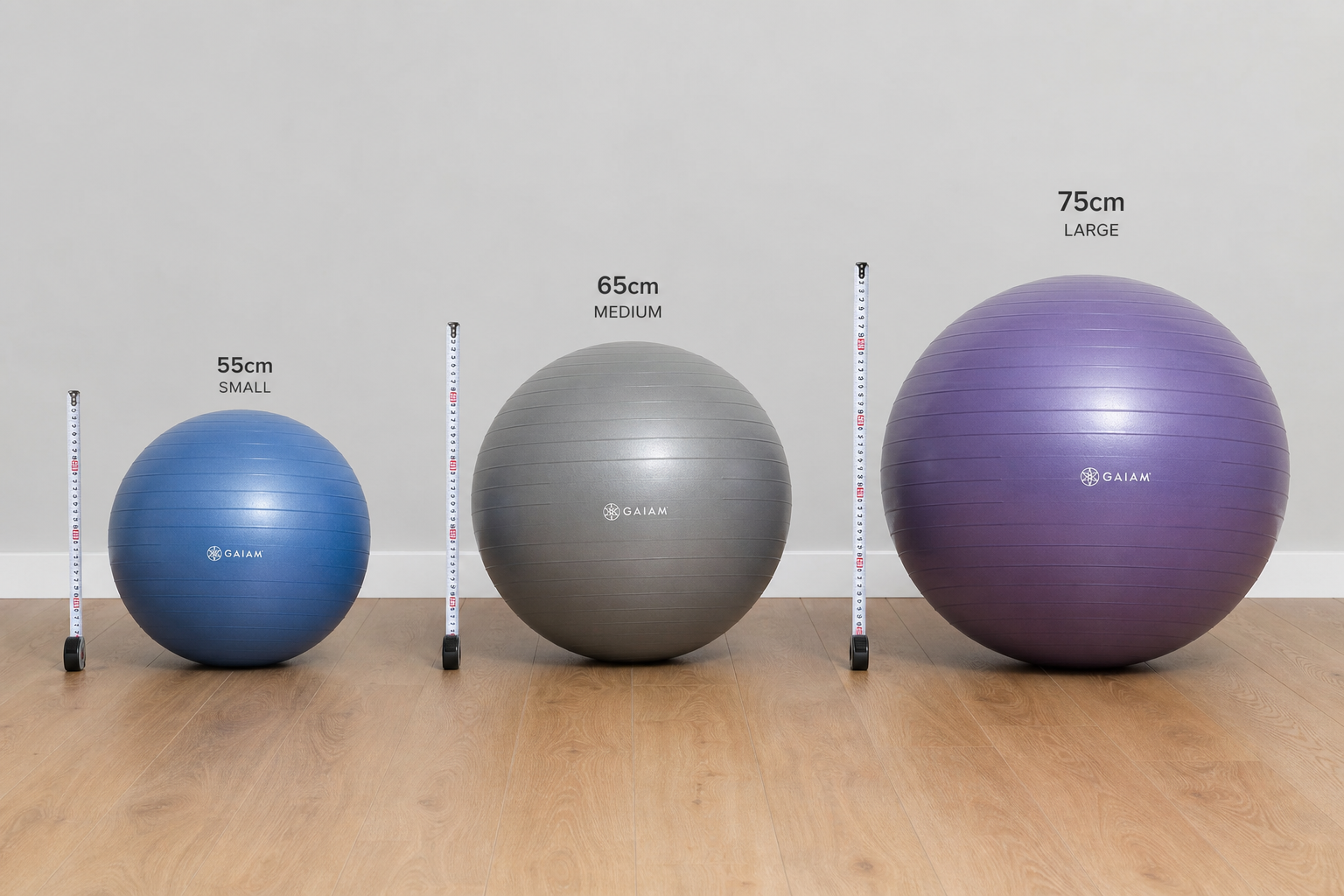 Three stability balls of different sizes lined up next to height markers on a wooden floor